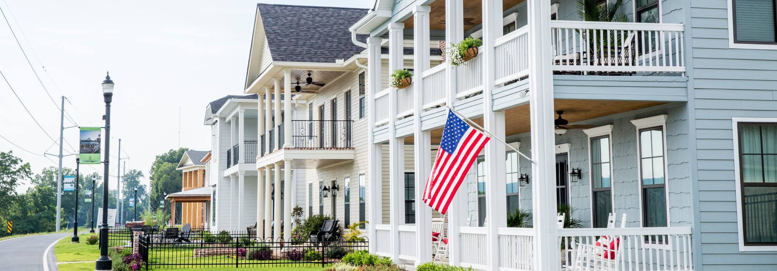 An American Flag sits just off a porch of a white building.